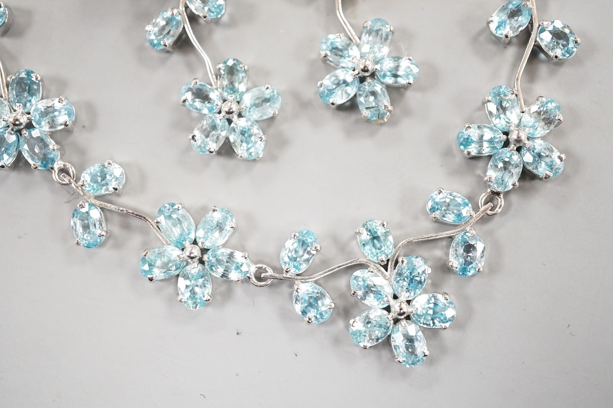 A modern 925 and blue zircon suite of jewellery, comprising a flower head cluster necklace and a pair of matching earrings.